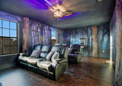 large haunted forest themed theatre room with a popcorn machine, two large couches, and black lights