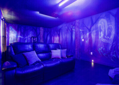 large haunted forest themed theatre room with a popcorn machine, two large couches, and black lights
